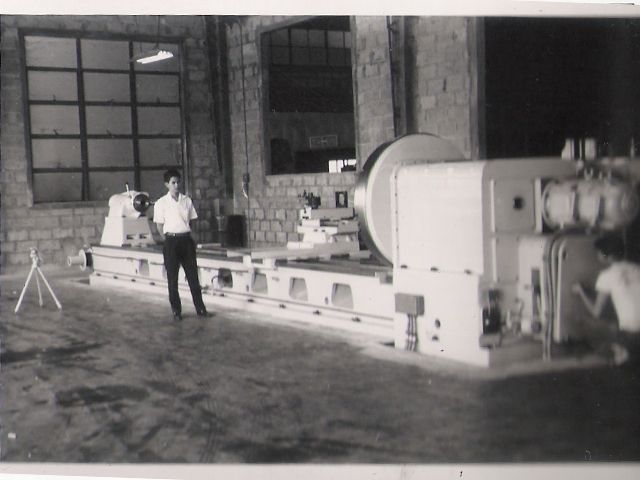 A very long industrial machine tool in a brick-walled hall, a man standing beside it