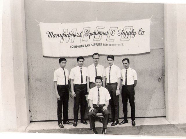 Men in white shirts and ties posed under a painted company banner