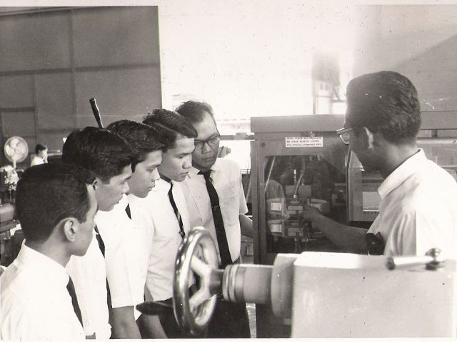 A group of young men crowded around an instructor at a lathe